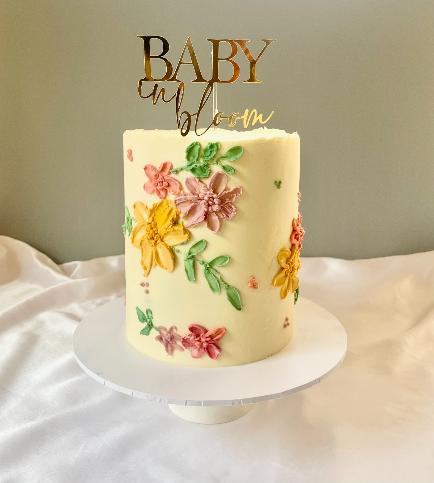 A cream baby shower cake with hand-piped flowers and a Baby in Bloom topper