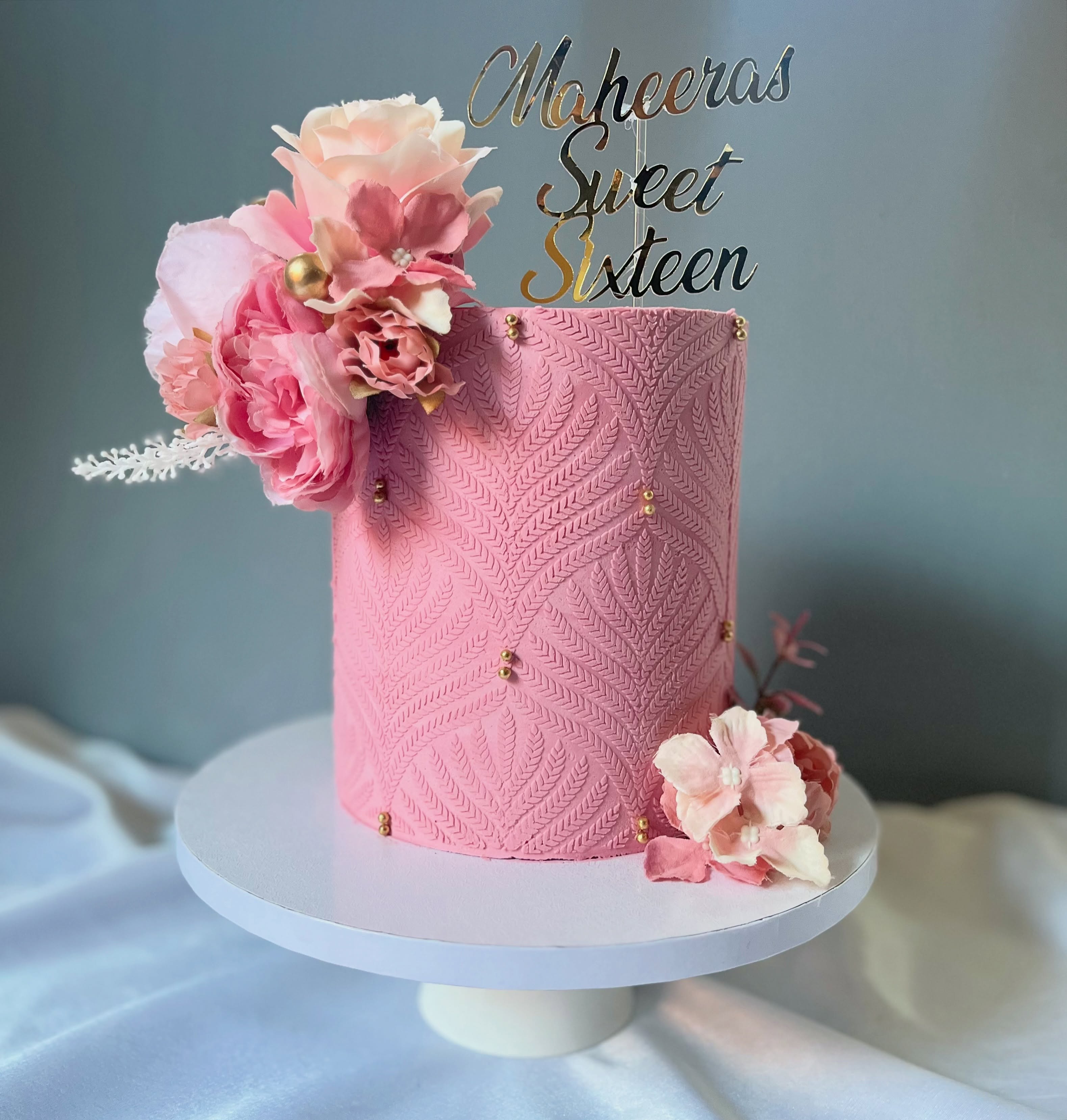A pink Sweet Sixteen cake with stencil work and fresh flowers