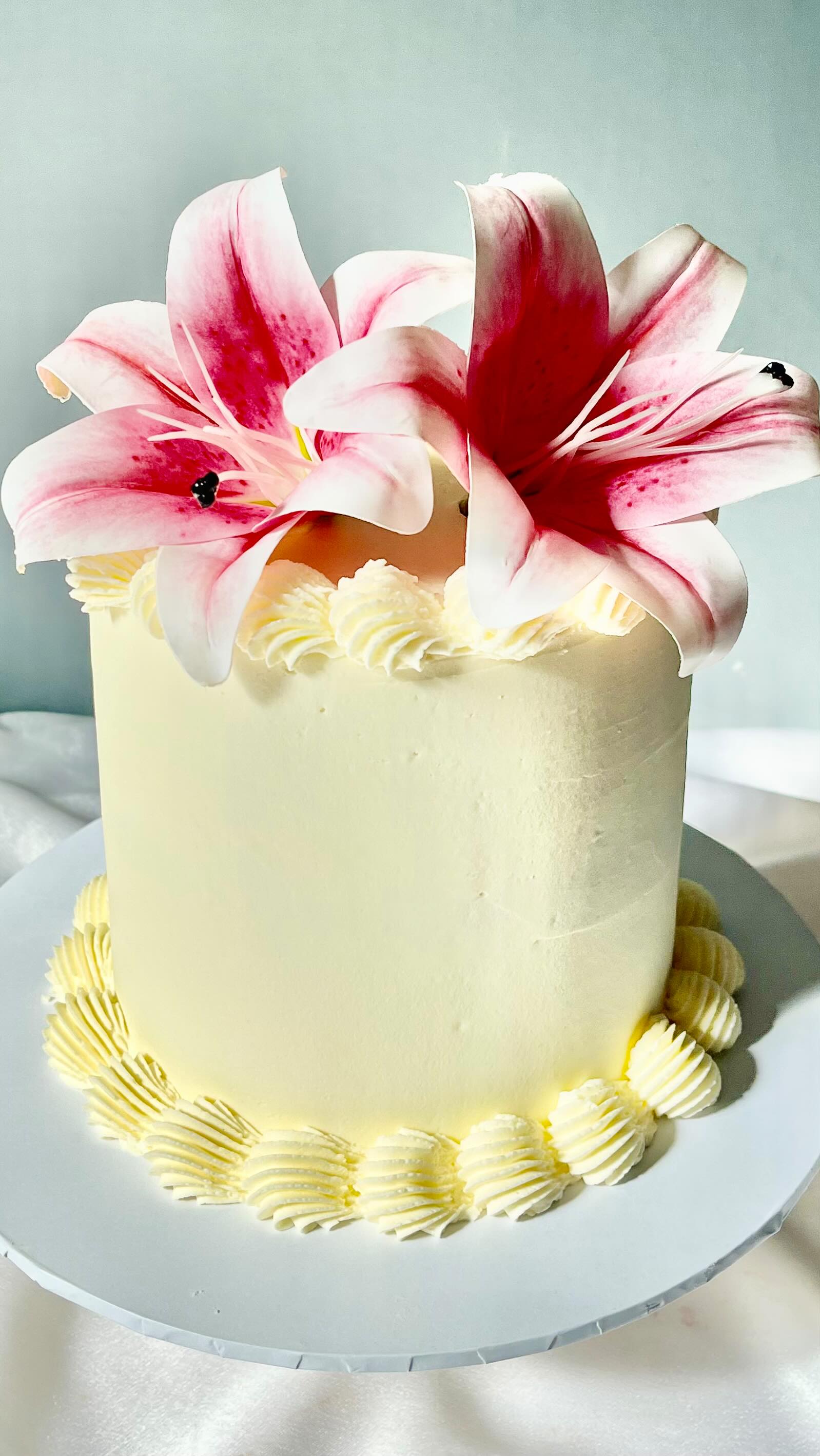 A cream cake topped with fresh pink lilies by Neily's Cakes